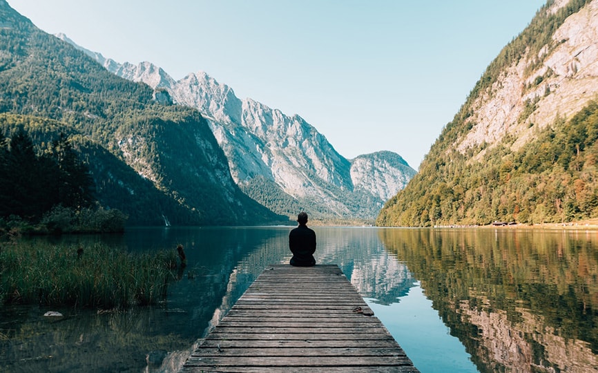 man sitting near mountains and lake